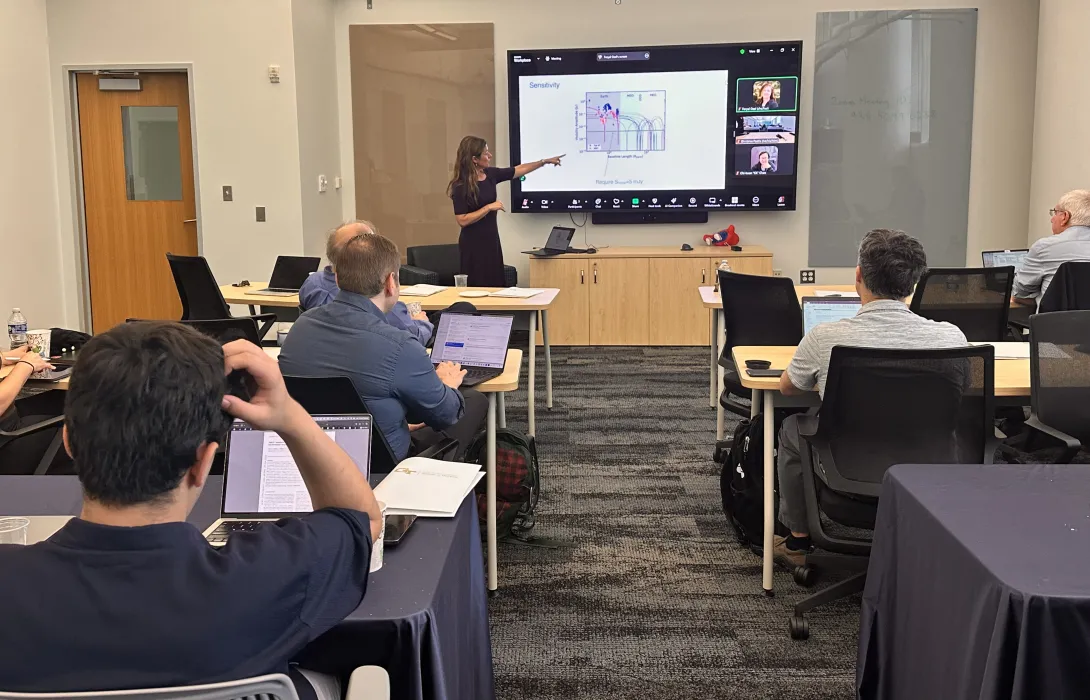 Image of classroom with woman pointing at a screen with full class in front of her.