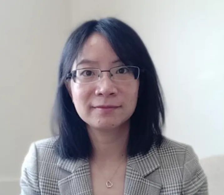 A headshot of a woman with black hair, glasses, and a gray plaid blazer