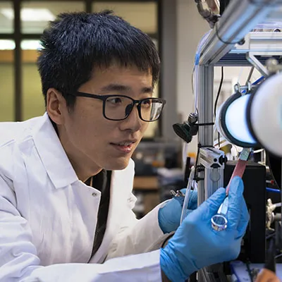 researcher with a white coat looking into a microscope