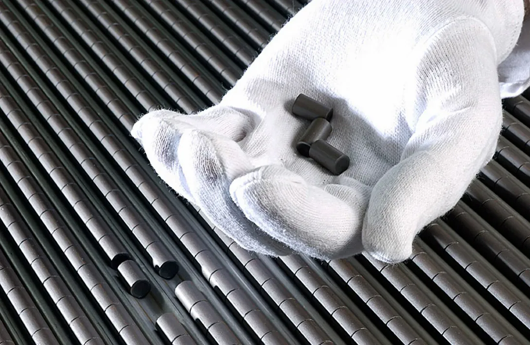 A white gloved hand holds 3 nuclear pellets with rows of nuclear pellets in the background