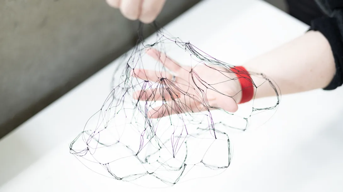 One hand holding a net of thin black cord in the middle. The net is draped over the person's other hand, below.