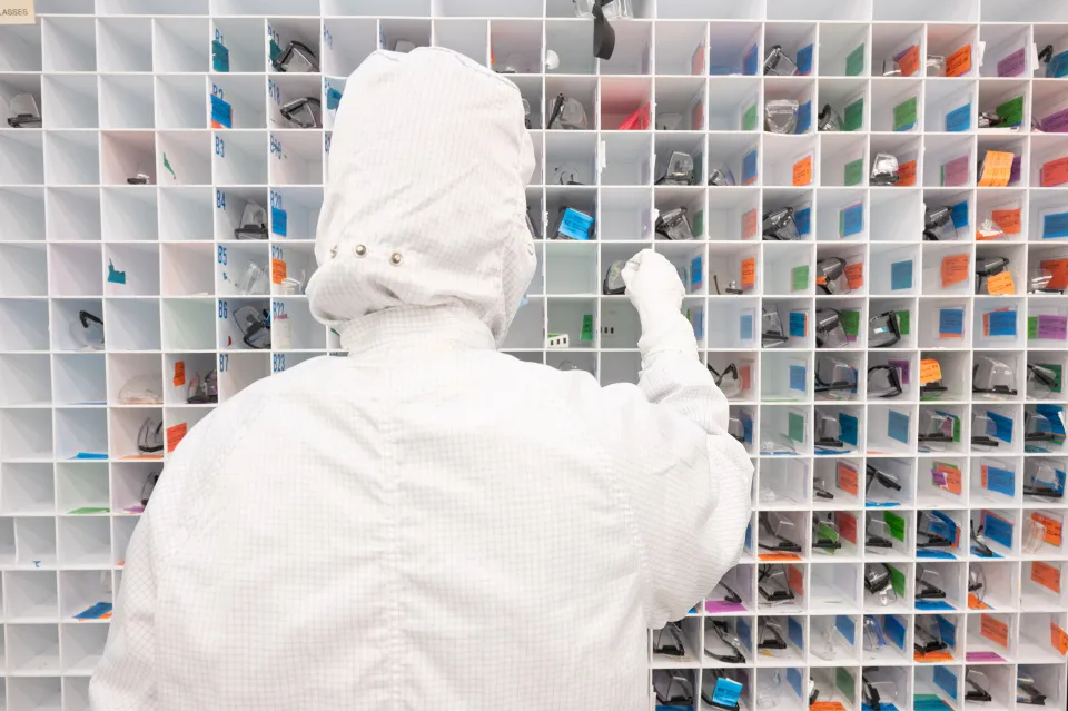 Person in cleanroom gear selecting glasses