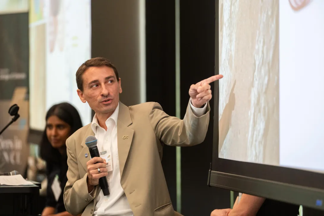 Professor James Wray holds microphone and points to powerpoint slide during his presentation