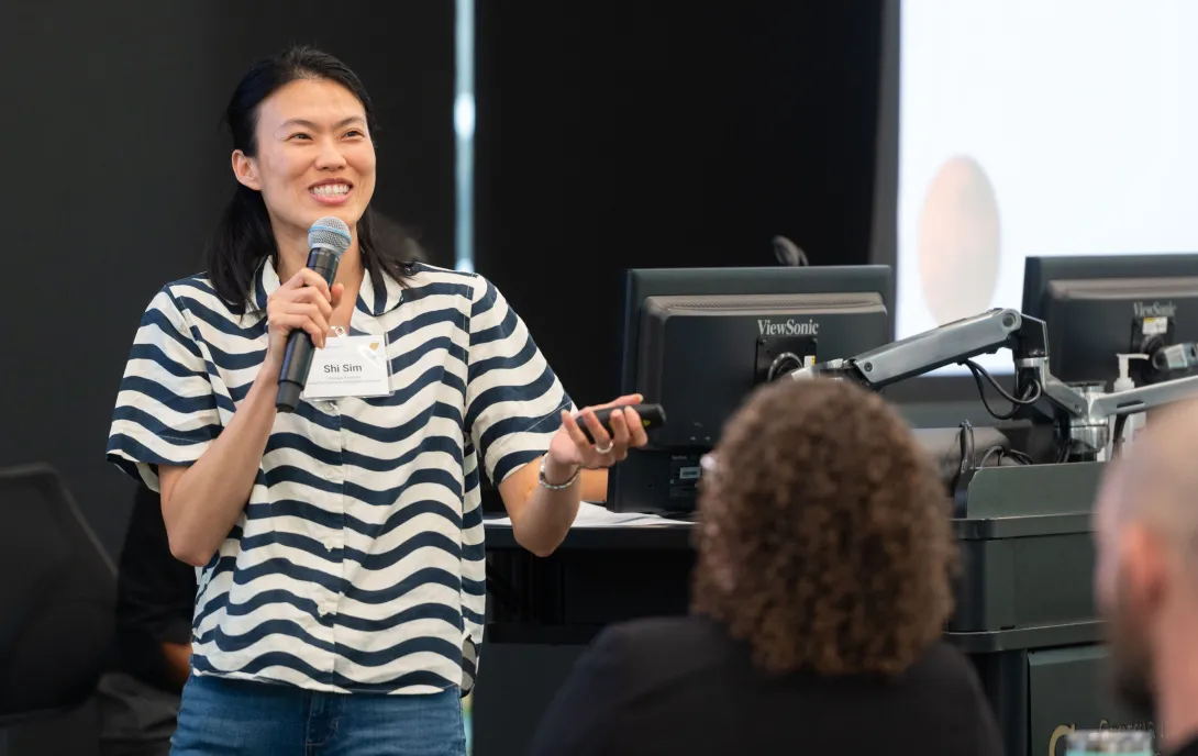 Joyce Shi Sim holds a microphone and laser pointer while presenting to room of people