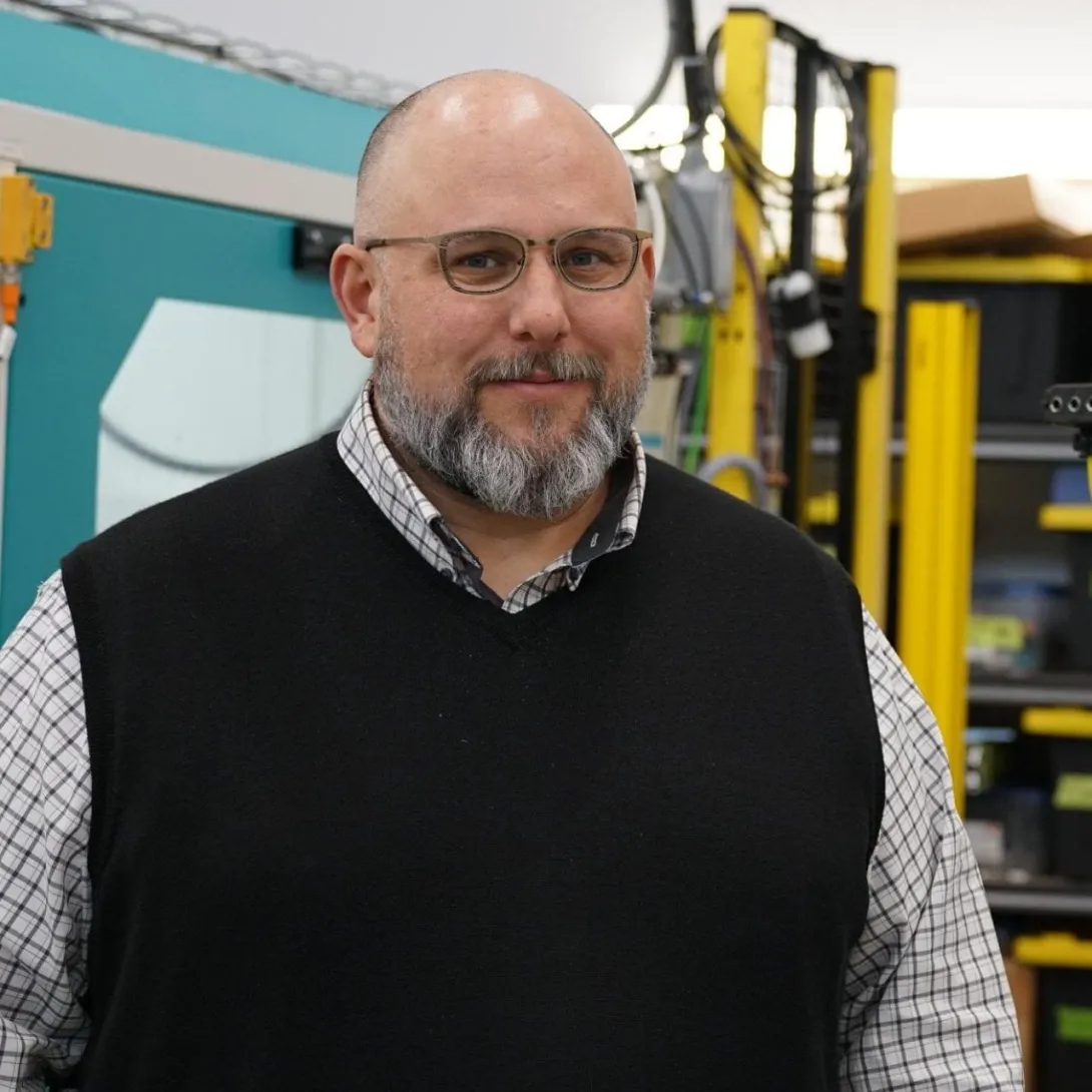A man with glasses and a beard in a dark vest and dress shirt