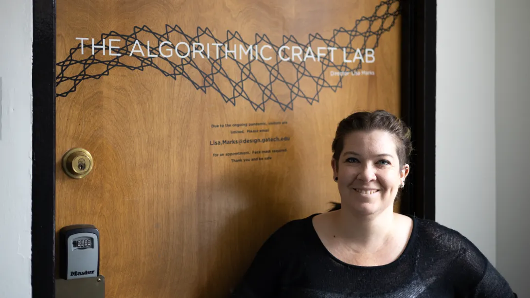 Lisa Marks standing in front of a closed door. The door features a net pattern and the title, "The Algorithmic Craft Lab."