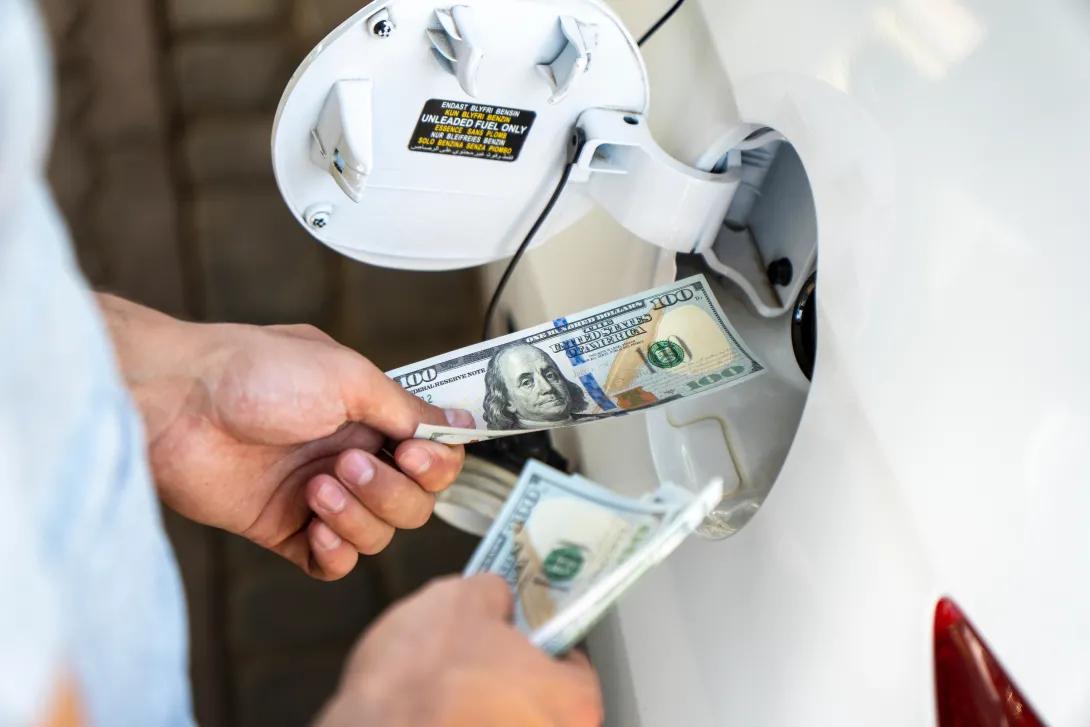 Hand of the man putting money into the opening gas tank of his car. Refueling car with gasoline at gas stations. 