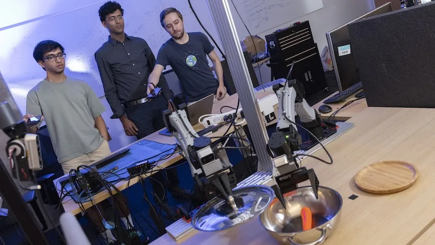 Three men use their phones to control a robot arm