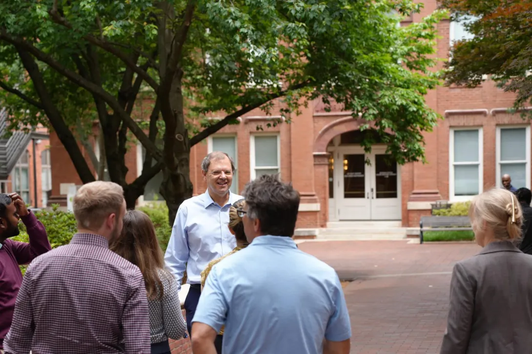 Joel Kostka and co-presenters stand under a leafy tree in a courtyard outside the RBI 2026 Spring Workshop.