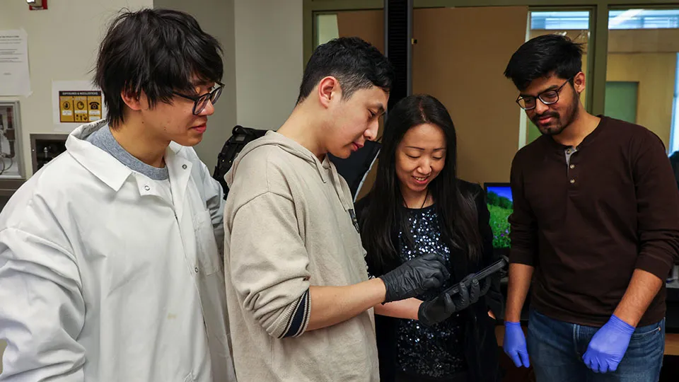 Associate Professor Yuhang Hu and three male students from her lab gather around and look at a soft adhesive hydrogel they are studying.