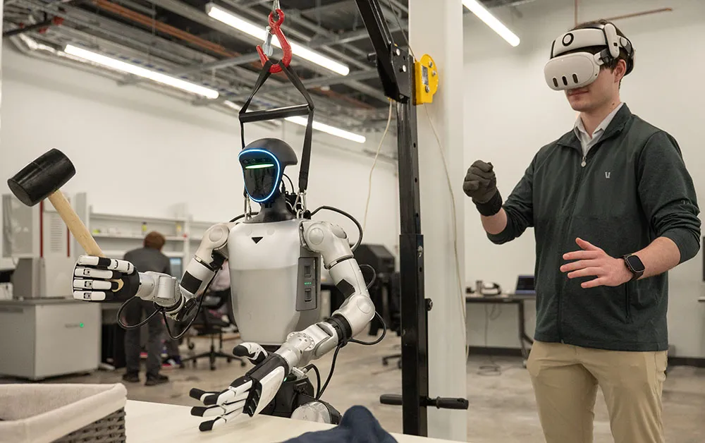 Person wearing a virtual reality headset controlling a humanoid robot equipped with tools in a laboratory setting.
