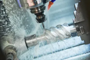 Close-up of a metal workpiece being cut by a rotating machining tool, with liquid coolant spraying around the cutting area.