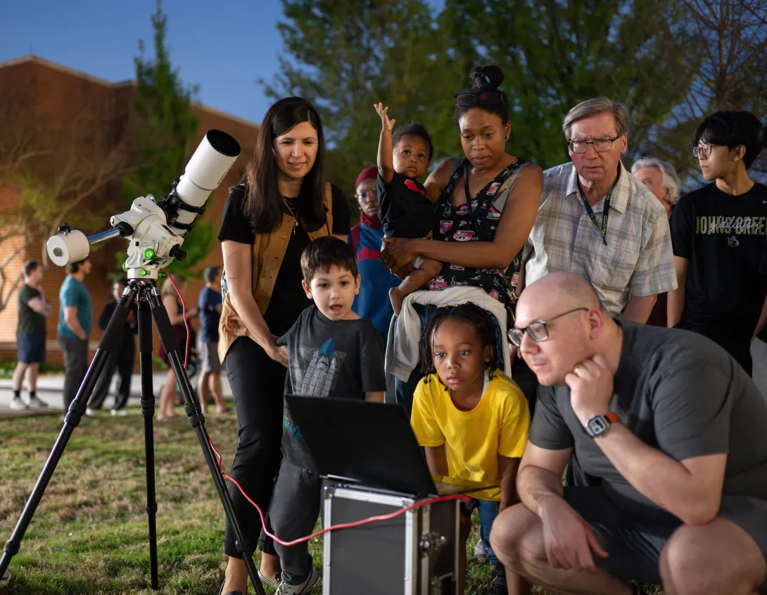 Adults and children observing the night sky through a computer that is connected to a telescope