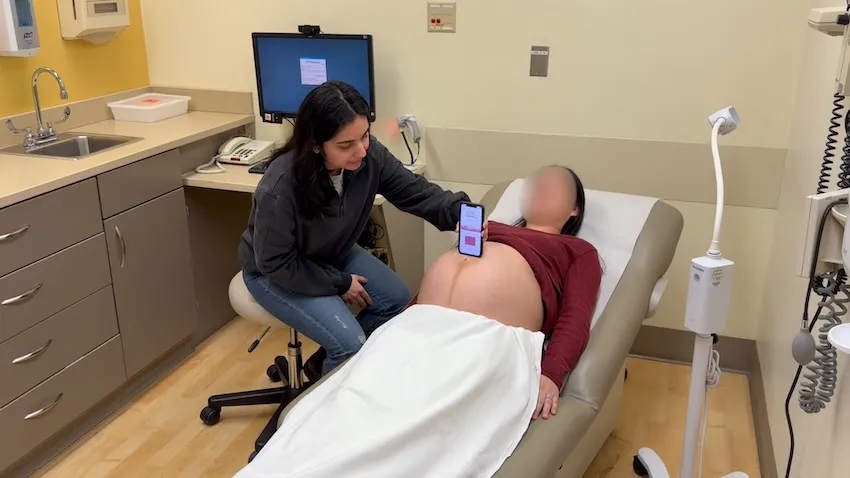 Woman holds mobile phone to the belly of a pregnant woman