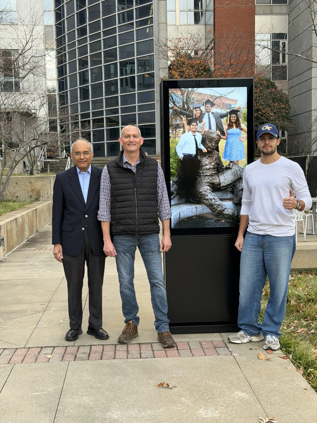 Left to Right: Dr. Joshi, Mike Brown and Maxium Belinon standing beside an outdoor display