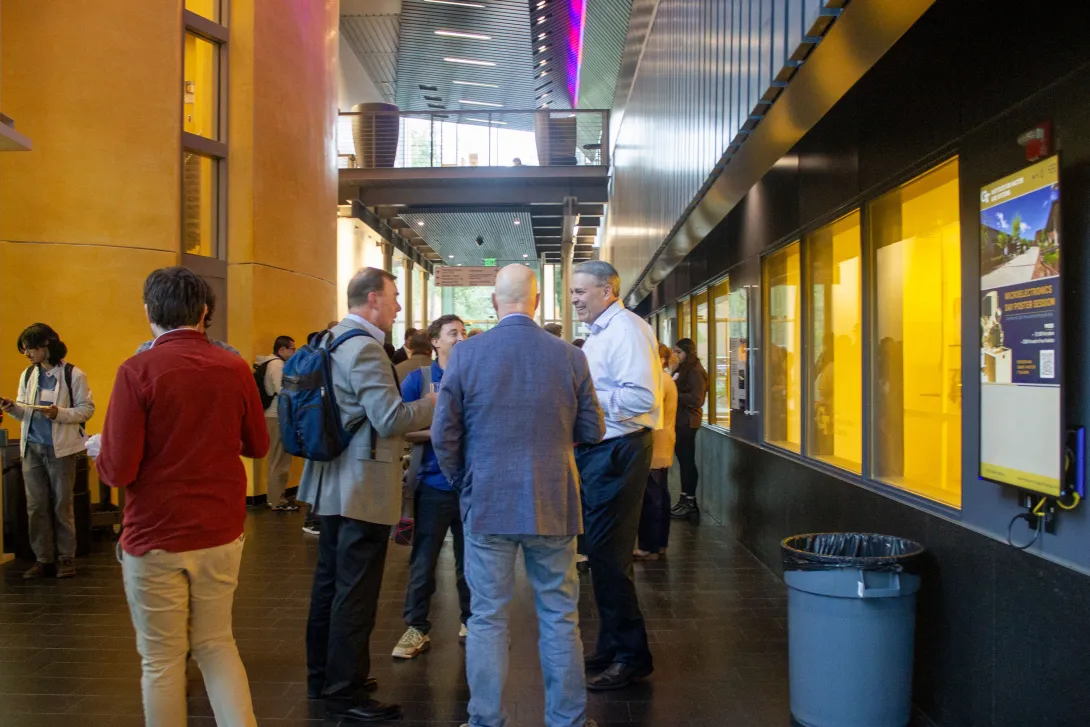 Attendees gather and talk in the Marcus Nanotechnology building lobby with gold walls, glass-fronted rooms, and a digital display.