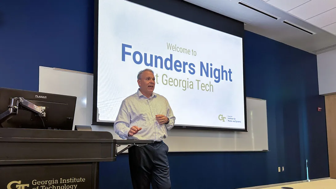 Eric Vogel speaks at a lectern in front of a screen reading “Welcome to Founders Night at Georgia Tech,” with Institute for Matter and Systems branding.