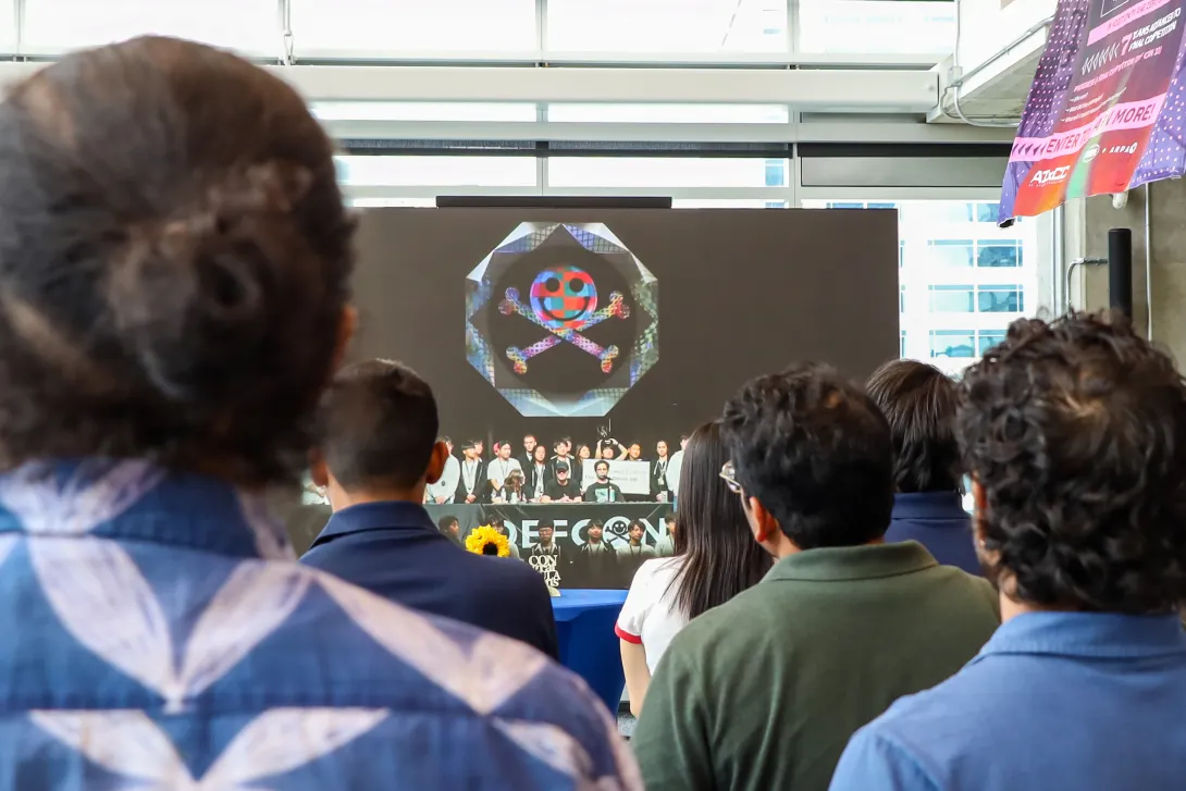 A crowd of people looking at a screen. The screen shows a team photo of Team Atlanta.